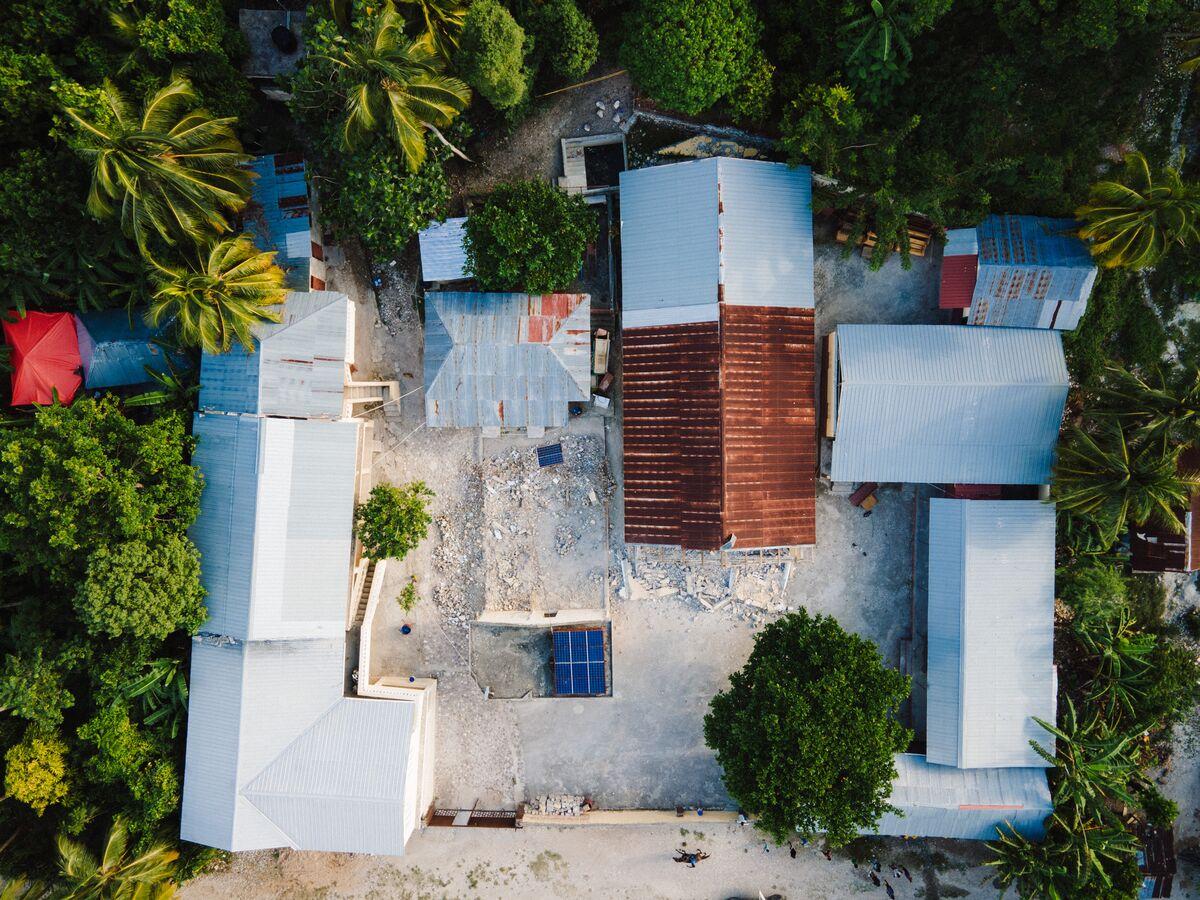 An aerial view of a group of metal-roofed buildings \ arranged in a rectangle, likely a local church that is \ partnered with Compassion. Lush, dense trees surround the \ buildings.